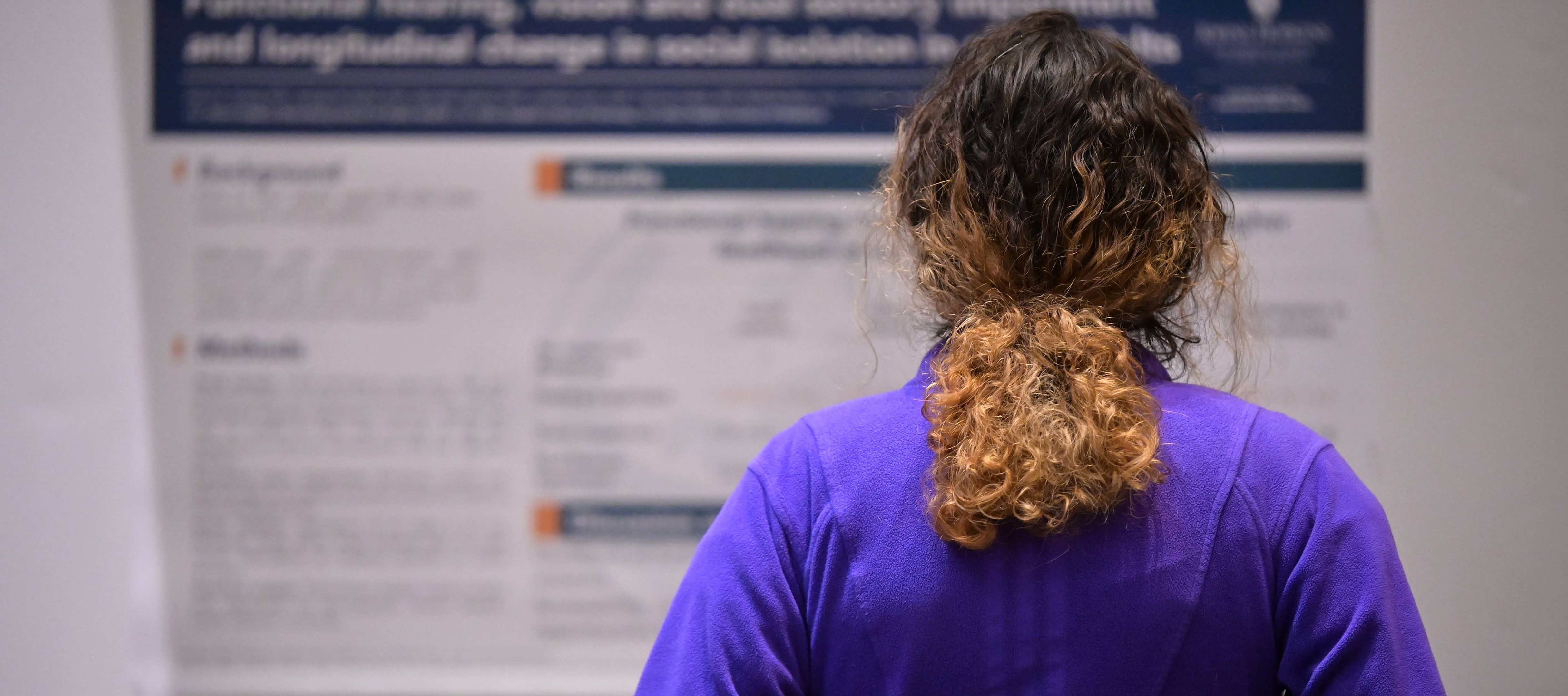 The back of clinician in a purple fleece, reading a research poster