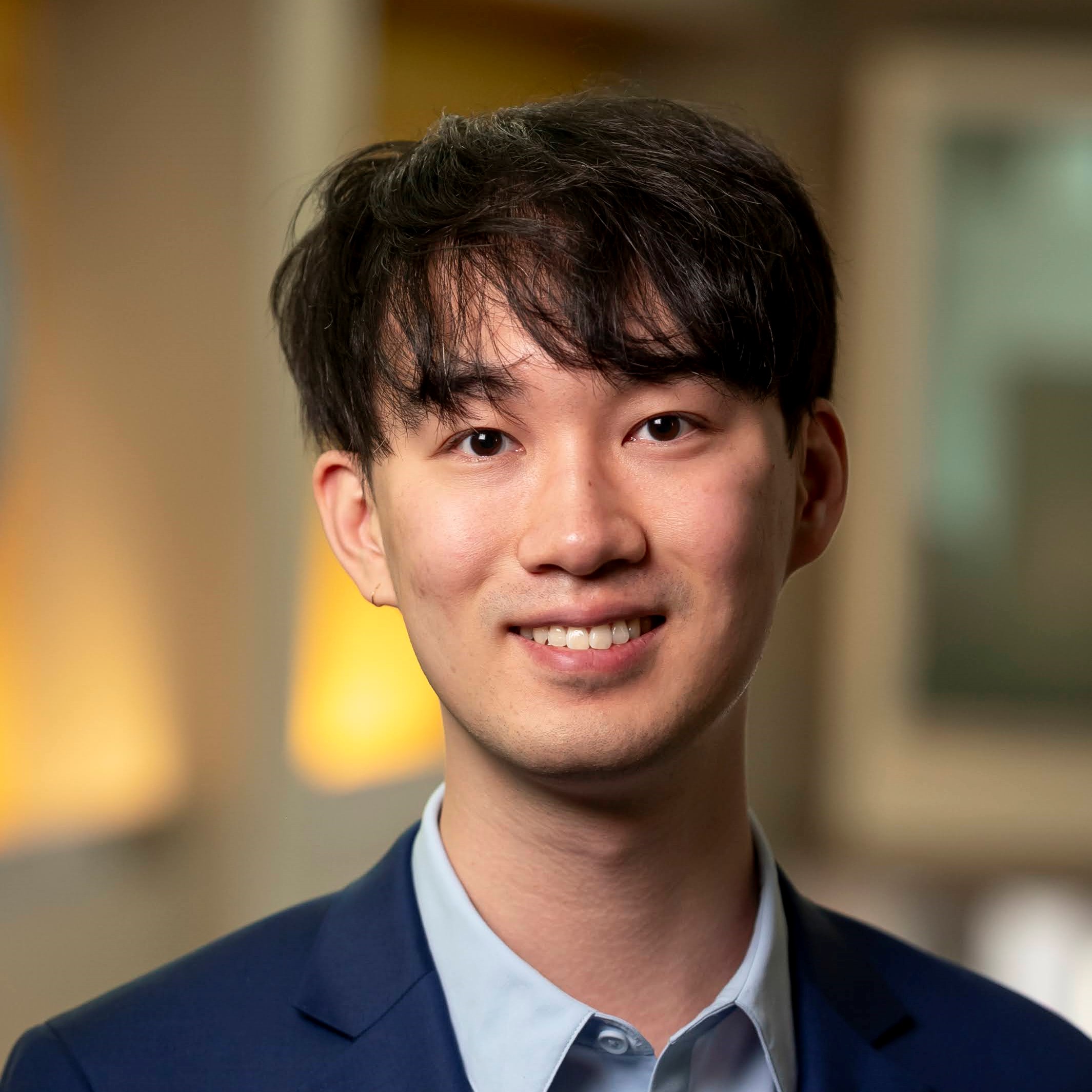 Wuyang Zhang smiles toward the viewer. He is wearing a blue blazer over a light blue collared shirt