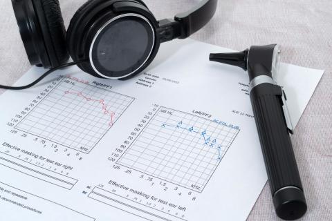 An otoscope and a pair of headphones rest on a printed audiogram